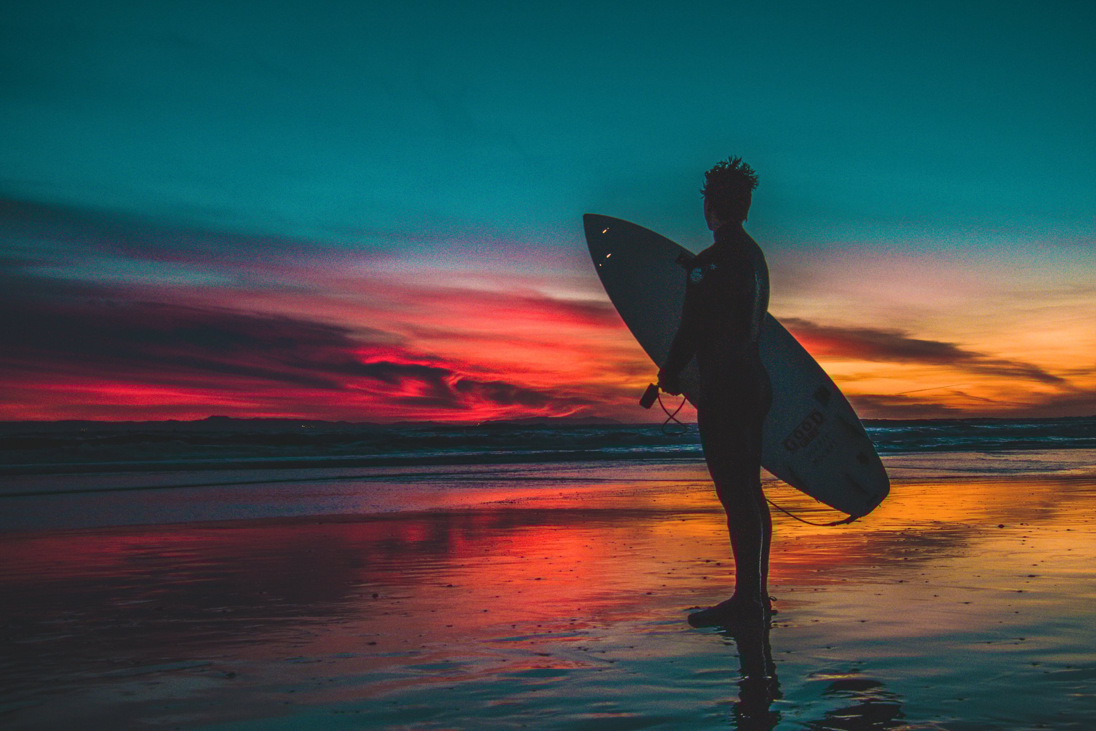 Silhouette of Man in Wet Suit Holding White Surfboard While Standing on Beach during Golden Hour